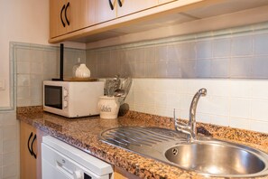 Eine Küche mit einer Granitabdeckung, einer Edelstahlspüle, einer Mikrowelle und einem Schrank mit Griff.