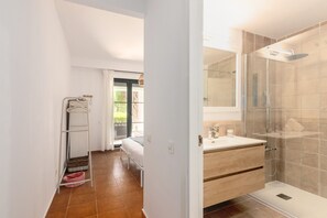 Een moderne badkamer met een glazen douchecabine, een wit wastafeltje en een houten opbergmeubel.
