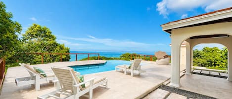 A poolside area with lounge chairs and a view of the ocean.