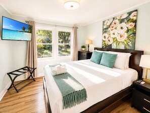 Ett hotellrum med en säng, en tv, en tavla, ett nattduksbord och ett fönster med gardiner.