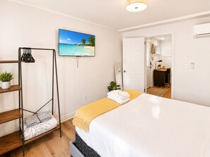 Ett hotellrum med en säng, en tv på väggen, en hylla med växter och en dörr som leder till ett badrum.