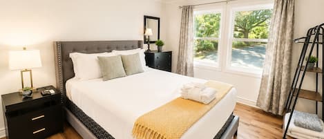 Una habitación de hotel con una cama, mesita de noche, lámpara y un ventanal con cortinas.