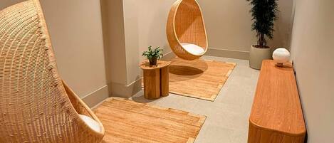 A modern interior with two hanging chairs, a wooden side table, a potted plant, and a rug.