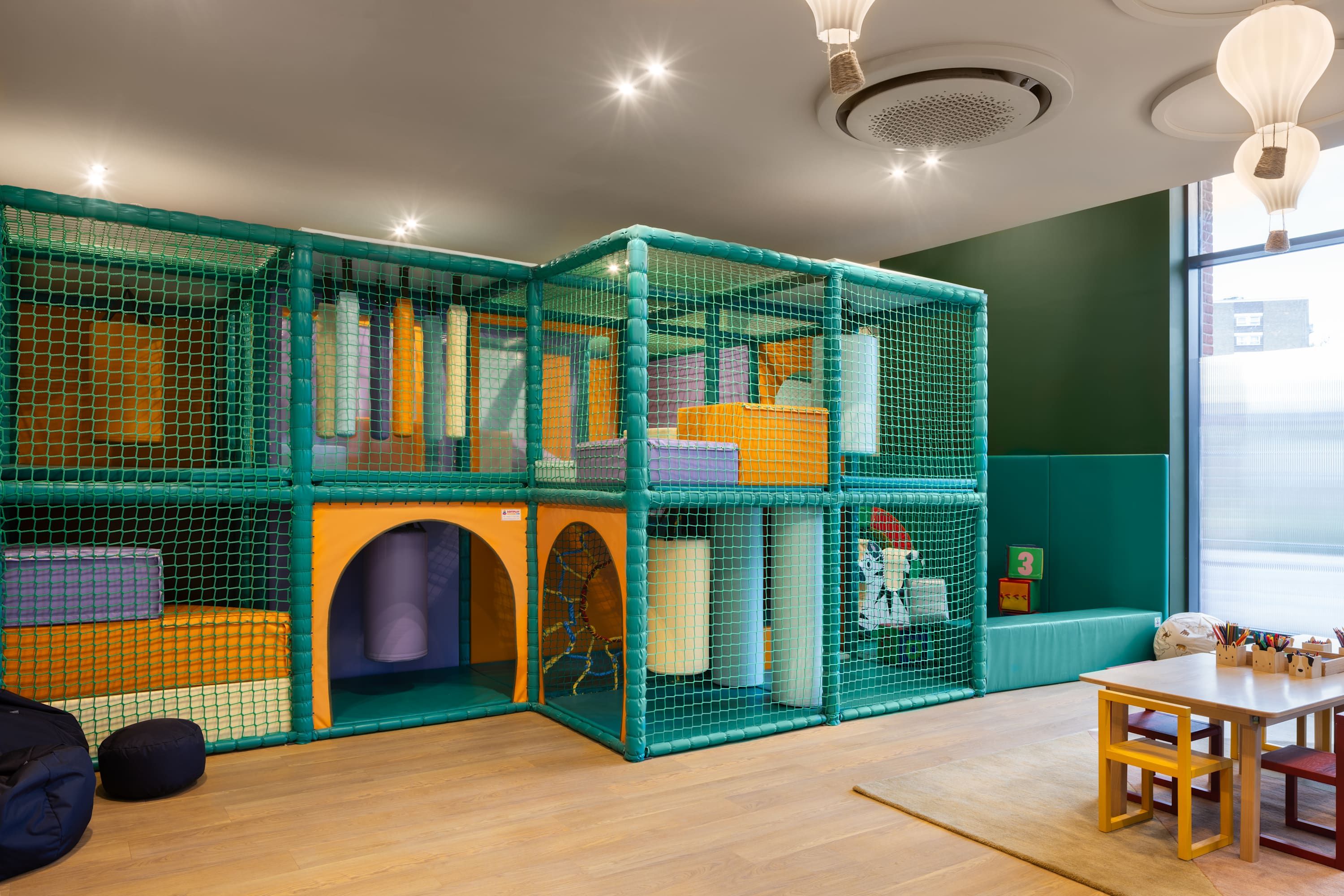 A play area with a netted enclosure, a table with chairs, and a window with a view of buildings.