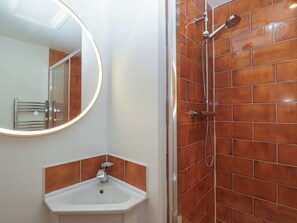 A bathroom with a white sink, a mirror with a light, and a shower with brown tiles. - Monnow (Abergavenny)