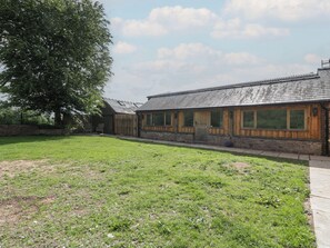A building with a sloped roof and large windows, surrounded by a grassy area and a tree. - Monnow (Abergavenny)