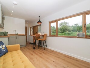 A modern kitchen with a dining area, a sofa, and a large window with a view of greenery. - Monnow (Abergavenny)