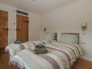 A bedroom with two beds, wooden doors, and a light-colored wall. - Monnow (Abergavenny)