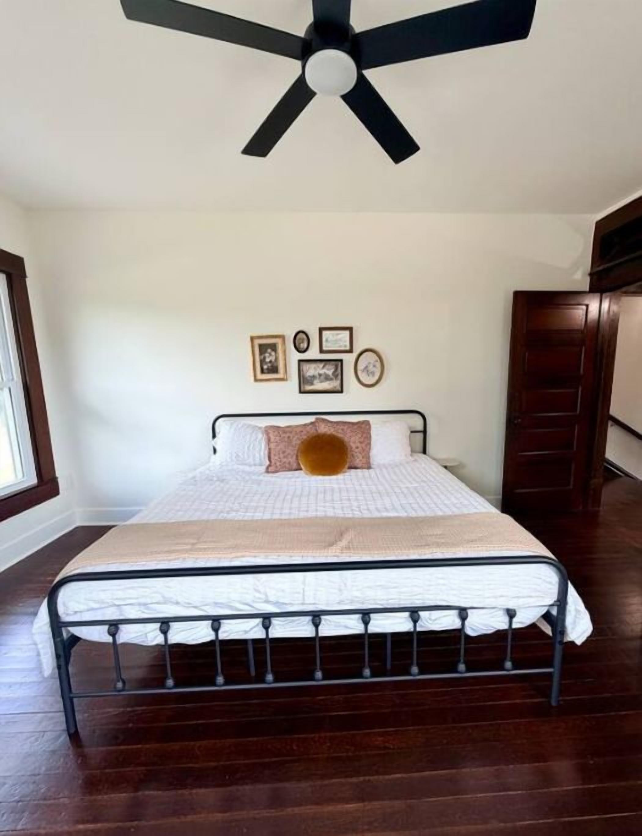 Een slaapkamer met een bed, een plafondventilator en een houten vloer.