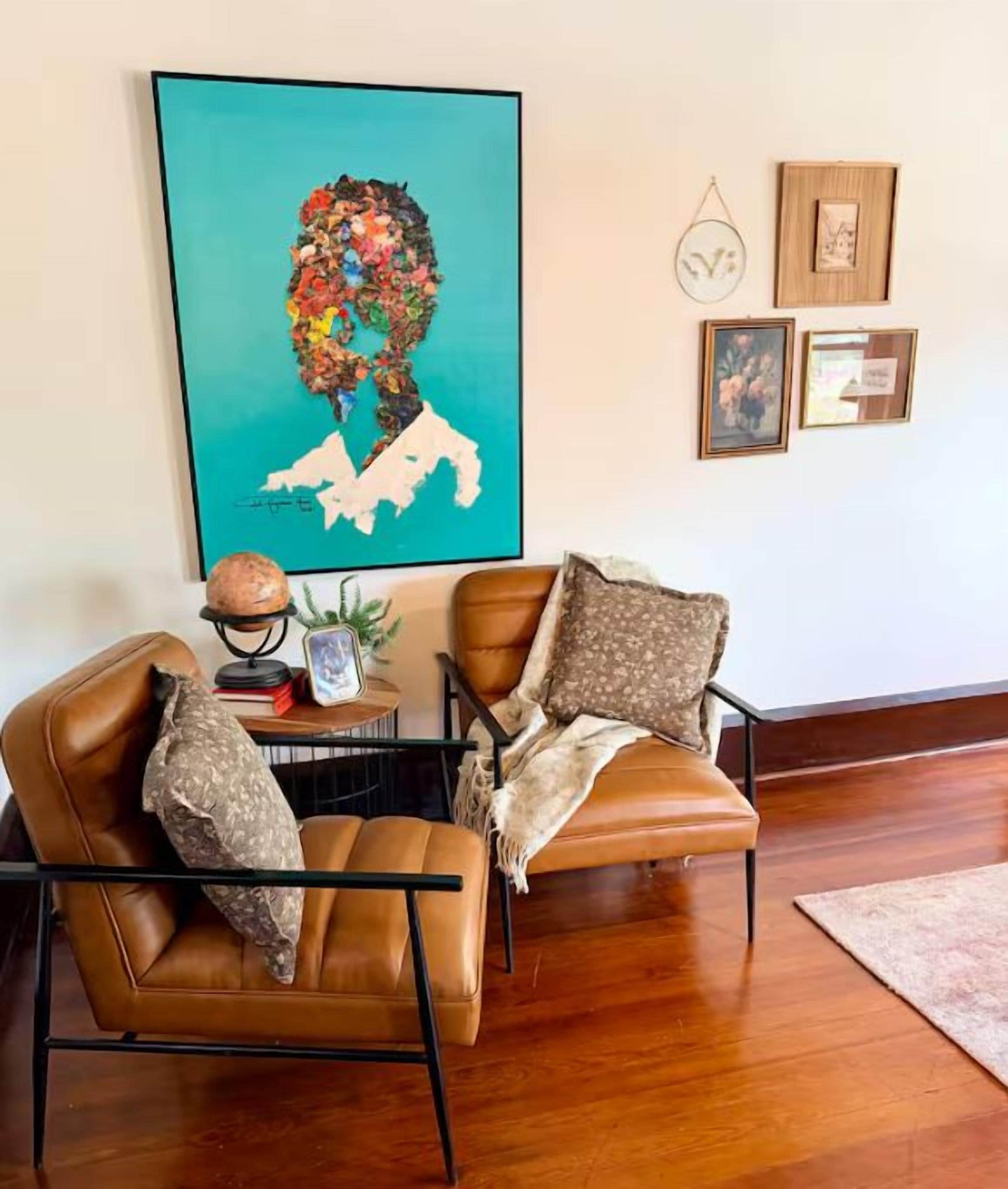 A living room with two brown leather chairs, a small round table with a globe and a framed picture, and a large abstract painting on the wall.