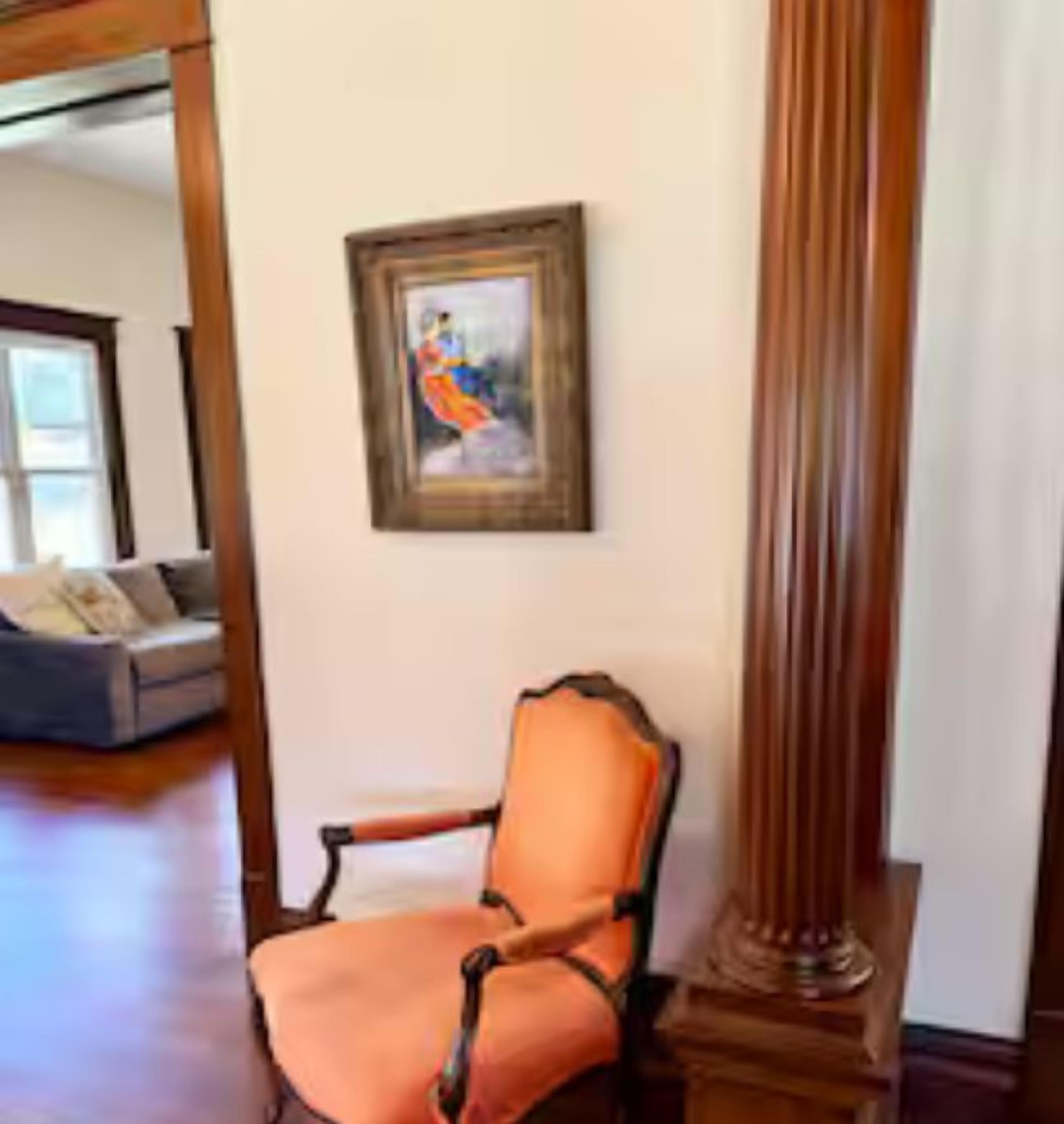 A room with a wooden chair, a framed painting, and a tall column.