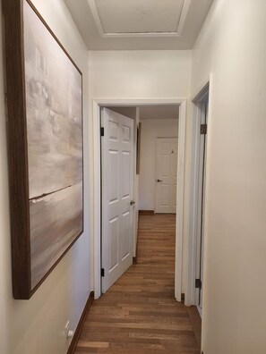 Un couloir doté d’un plancher en bois, de murs blancs et d’un grand tableau abstrait sur le mur de gauche.