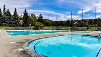 A swimming pool with clear blue water, surrounded by a paved deck and a metal fence.