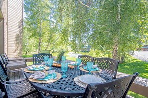 A round outdoor table set with chairs, surrounded by a wooden deck and a garden.