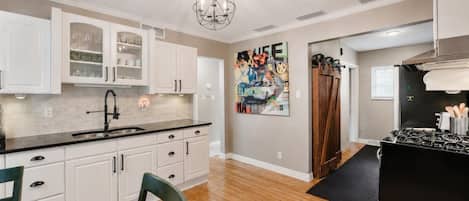A kitchen with white cabinets, a black countertop, a chandelier, and a painting on the wall.