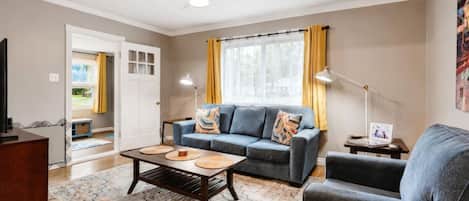 Una sala de estar con sofá, sillón, mesa de centro y televisor.