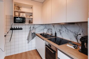 Uma cozinha moderna com armários brancos, painel de fundo em mármore, forno embutido e máquina de café.