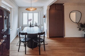 Un comedor con una mesa redonda, cuatro sillas, una lámpara colgante y un espejo grande en la pared.