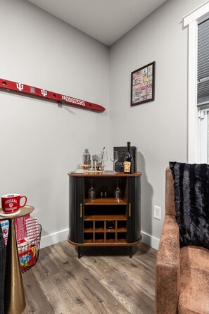 A corner room with a wooden cabinet, a red mug, a framed picture, and a black couch. - Hoosier Hideaway | King Bed, Beer Pong, Shotski (Bloomington)