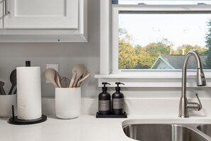 A kitchen with a stainless steel sink, a window with a view of trees, and toiletries on the counter. - Hoosier Hideaway | King Bed, Beer Pong, Shotski (Bloomington)