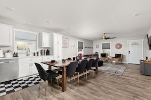 A modern kitchen with white cabinets, a dining area with a wooden table and black chairs, and a ceiling fan. - Hoosier Hideaway | King Bed, Beer Pong, Shotski (Bloomington)