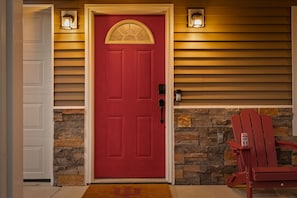 A red door with a stone wall and wooden siding, a mailbox, and a red Adirondack chair. - Hoosier Hideaway | King Bed, Beer Pong, Shotski (Bloomington)