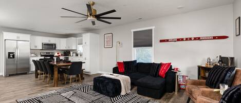 A modern living room with a black sofa, a coffee table, and a dining area with a wooden table and chairs.