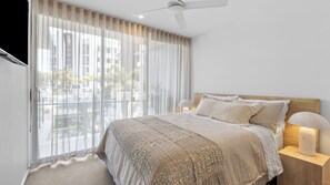 A bedroom with a large bed, a ceiling fan, a nightstand with a lamp, and sheer curtains. - Sol 601 - Coolangatta/ Kirra Luxury Apartment - Min. 3 Night Stays - Linen Provided (Coolangatta)