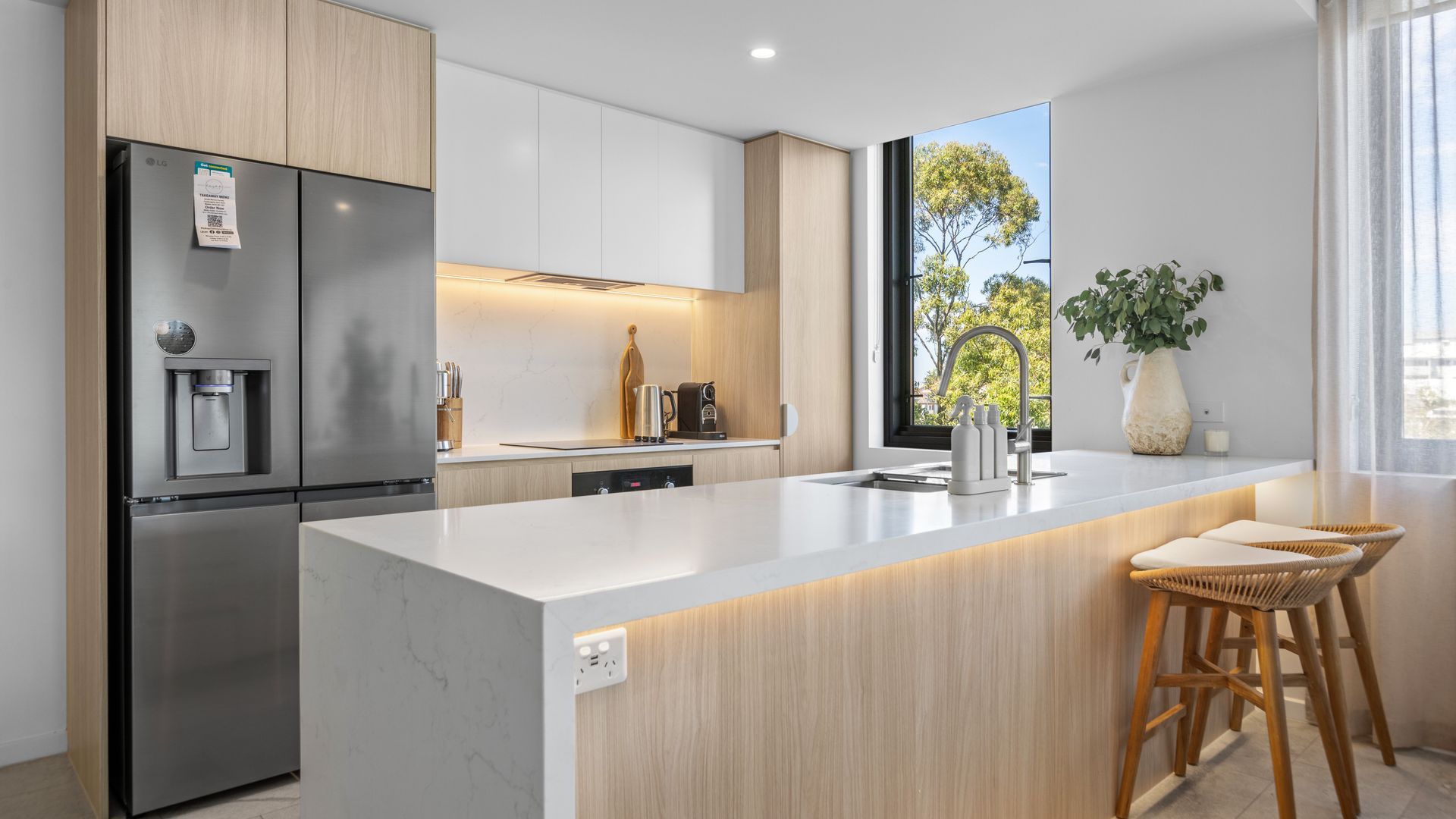 A modern kitchen with a built-in island, stainless steel appliances, and a large window offering a view of trees.