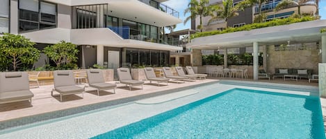 A modern hotel with a swimming pool, outdoor seating, and a view of the building's architecture.
