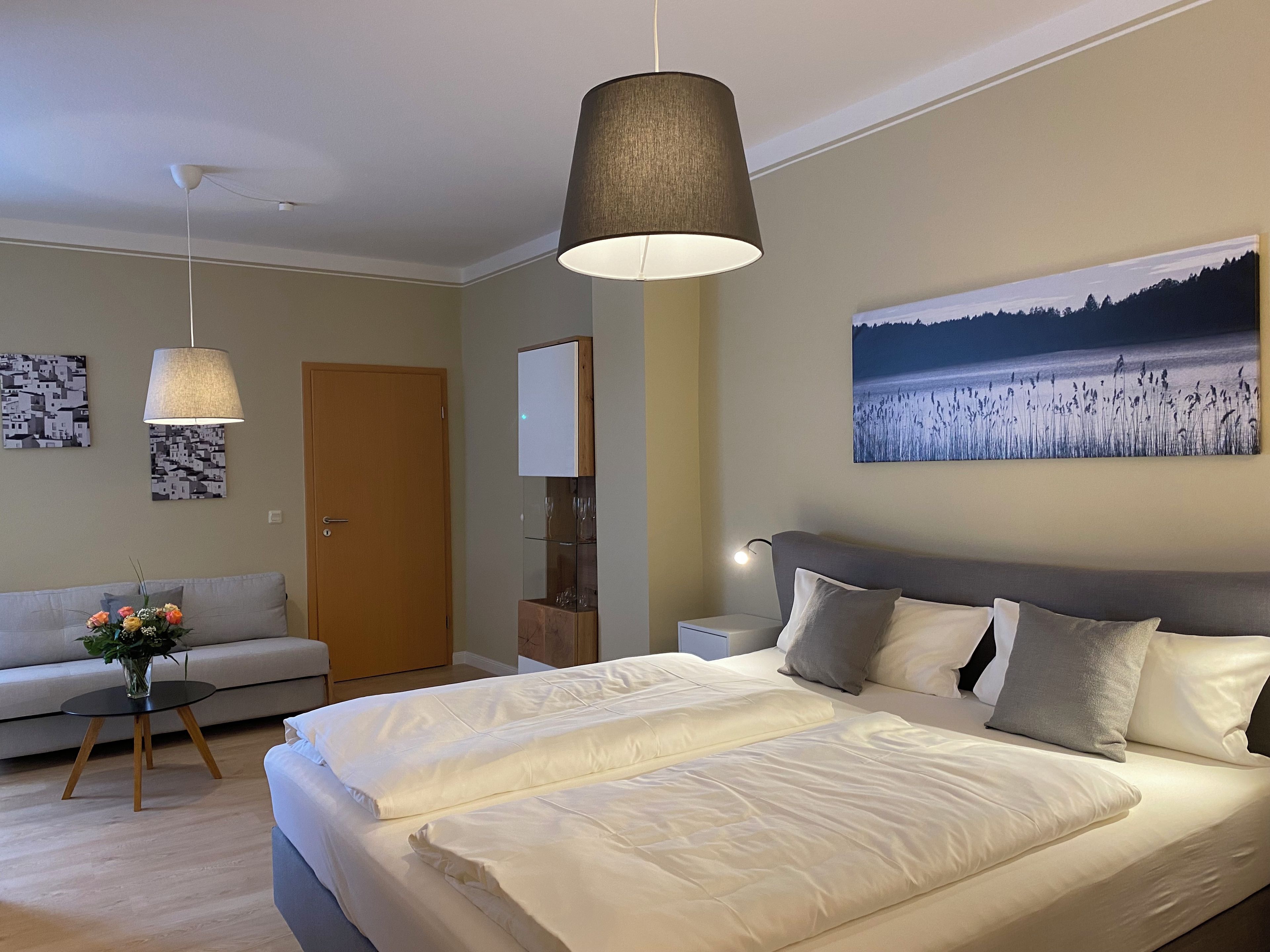 Ein Schlafzimmer mit einem großen Bett, einem Nachttisch, einer Nachttischlampe, einem Sofa und einer Tür.