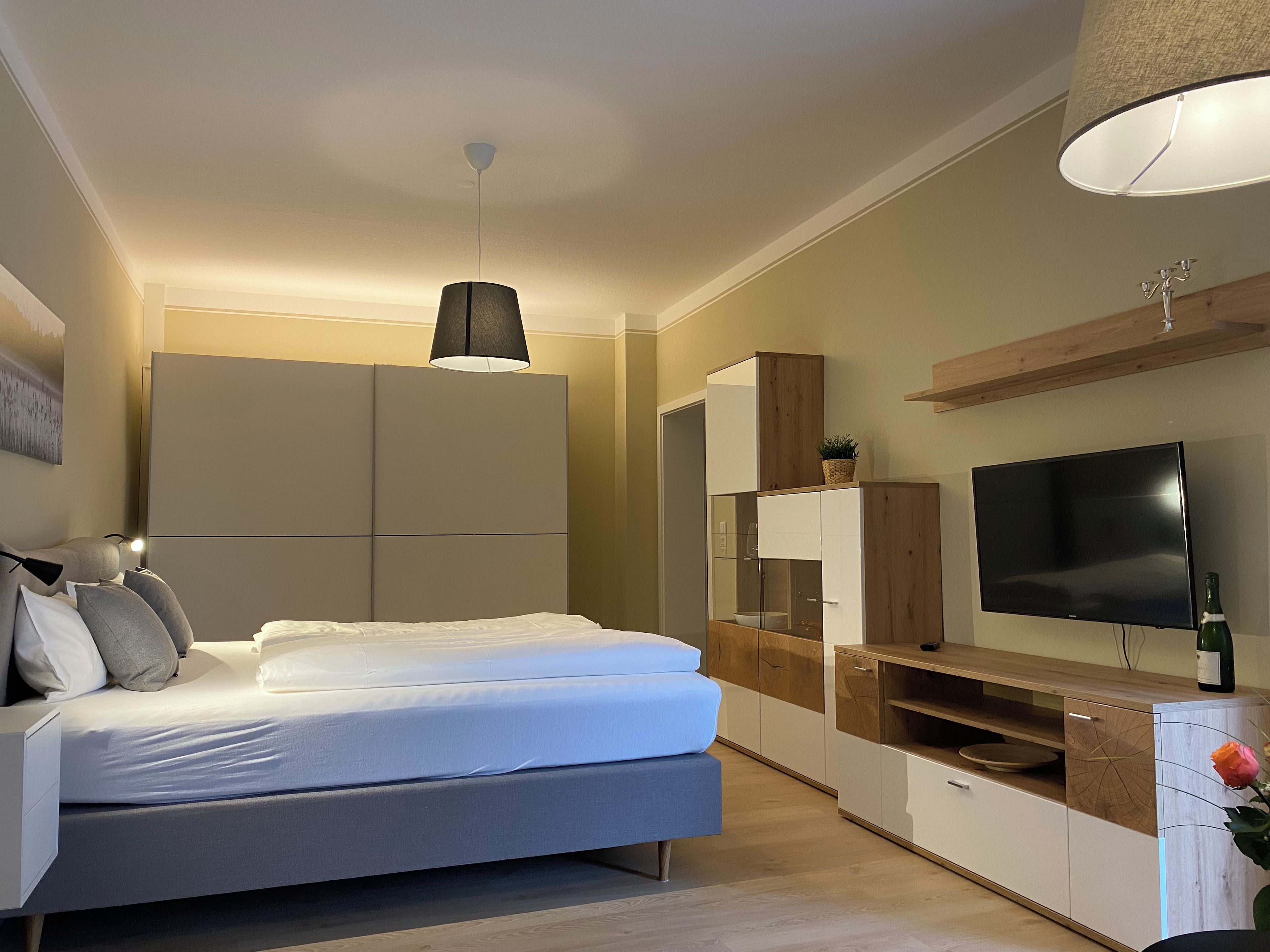 Een moderne slaapkamer met een bed, kast, televisie en een klein tafeltje met een fles.
