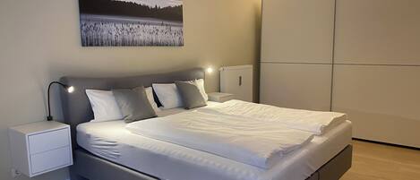 A modern bedroom with a large bed, bedside tables, a hanging lamp, and a painting on the wall.