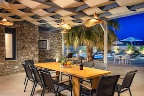 An outdoor dining area with a stone wall, a wooden table, and black chairs. - Villa Artemis Lindian Palm by Villa Plus (Lardos)