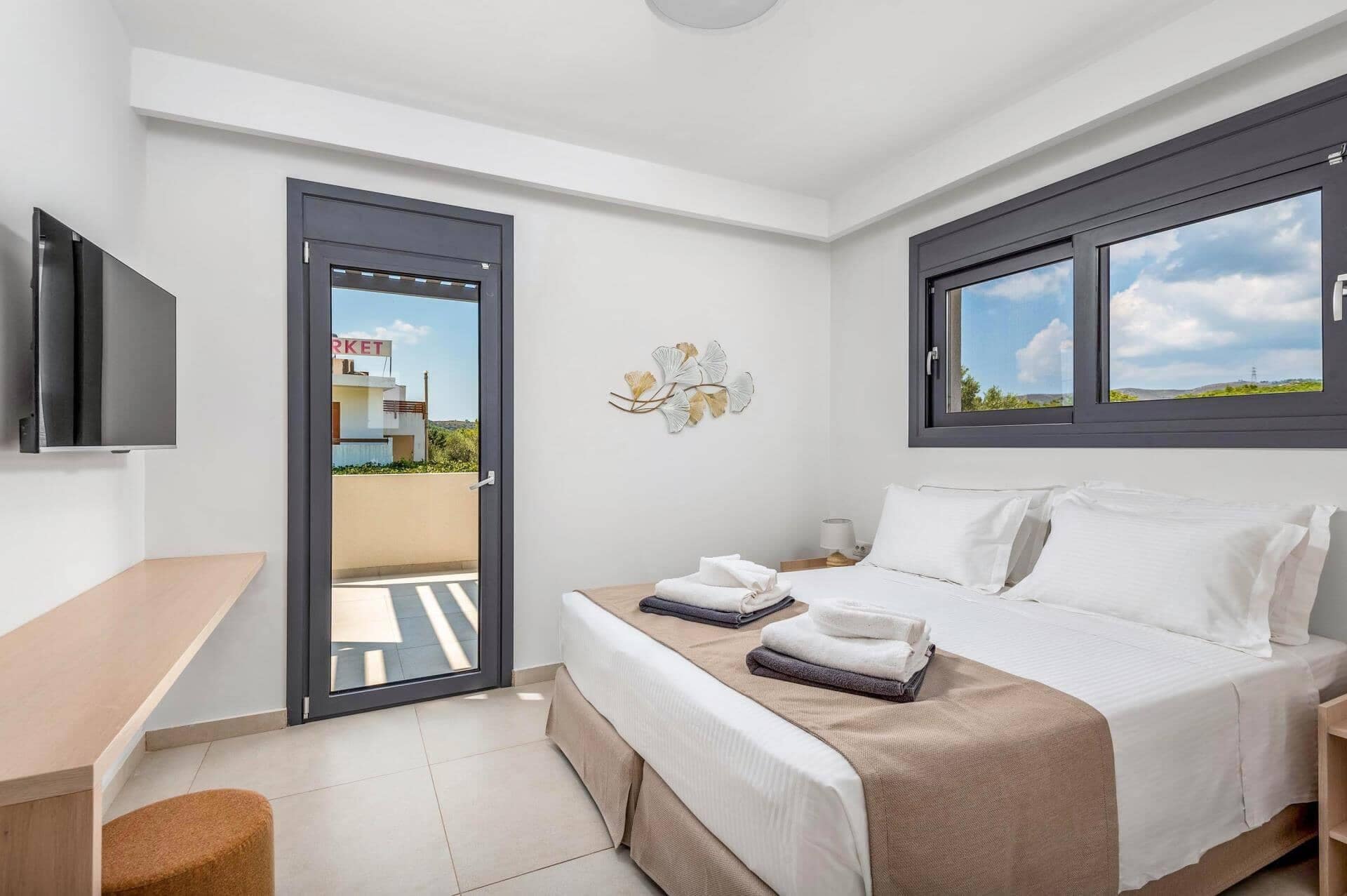 Une chambre d’hôtel équipée d’un lit, d’un bureau, d’une télévision, d’une fenêtre donnant sur un paysage agréable et d’une porte menant à l’extérieur.