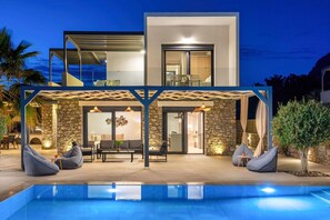 A modern two-story house with a swimming pool, outdoor seating, and a covered patio area. - Villa Artemis Lindian Palm by Villa Plus (Lardos)