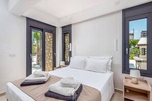 Een hotelkamer met een bed, twee ramen, een nachtkastje en uitzicht op buiten.
