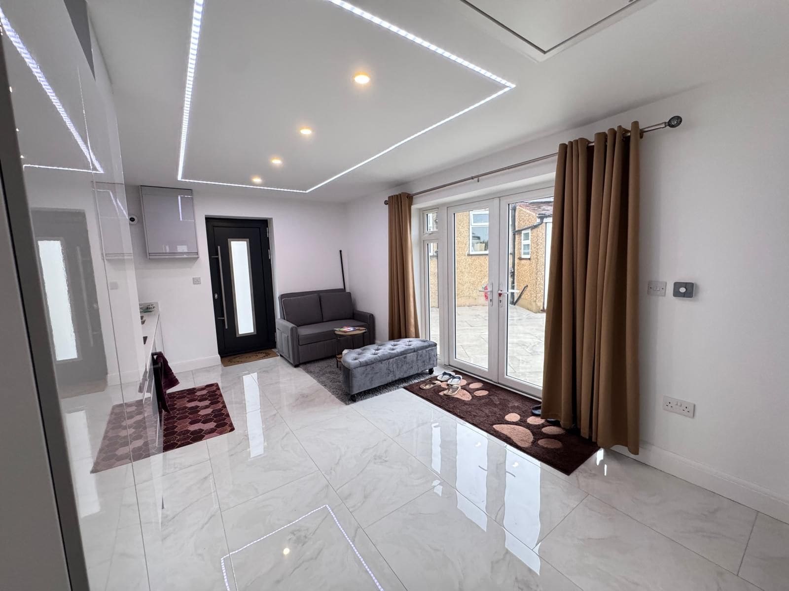 A modern interior with a glass door leading to a patio, a grey sofa, and a marble floor.