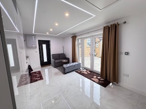 A modern interior with a glass door leading to a patio, a grey sofa, and a marble floor. - Self-contained Independent beautiful apt (Northolt)