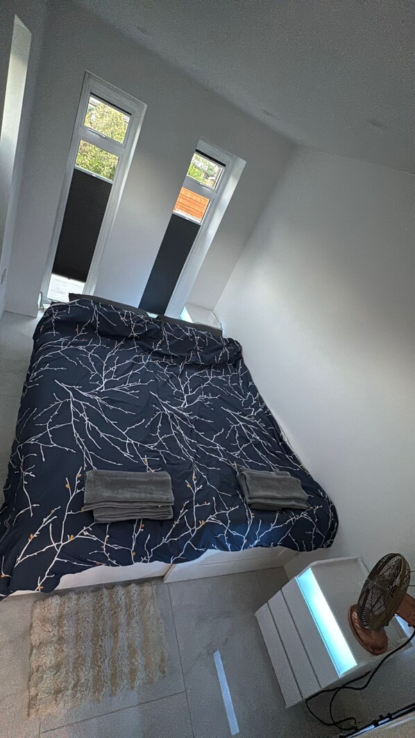 A bedroom with a bed, two windows, and a fan.