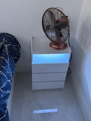 A bedside table with a fan and a drawer unit. - Self-contained Independent beautiful apt (Northolt)