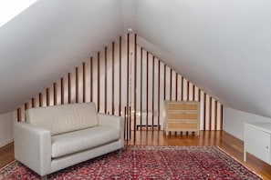 A room with a sloped ceiling, a sofa, a patterned rug, a cabinet, and vertical wooden panels. - Villa Casa da Tia by Villa Plus (Machico)
