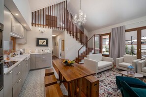 A modern kitchen with a wooden dining table and benches, a staircase with wooden railings, and a living area with sofas and a coffee table. - Villa Casa da Tia by Villa Plus (Machico)