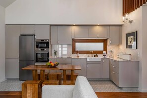A modern kitchen with grey cabinets, a wooden dining table, and a built-in oven. - Villa Casa da Tia by Villa Plus (Machico)