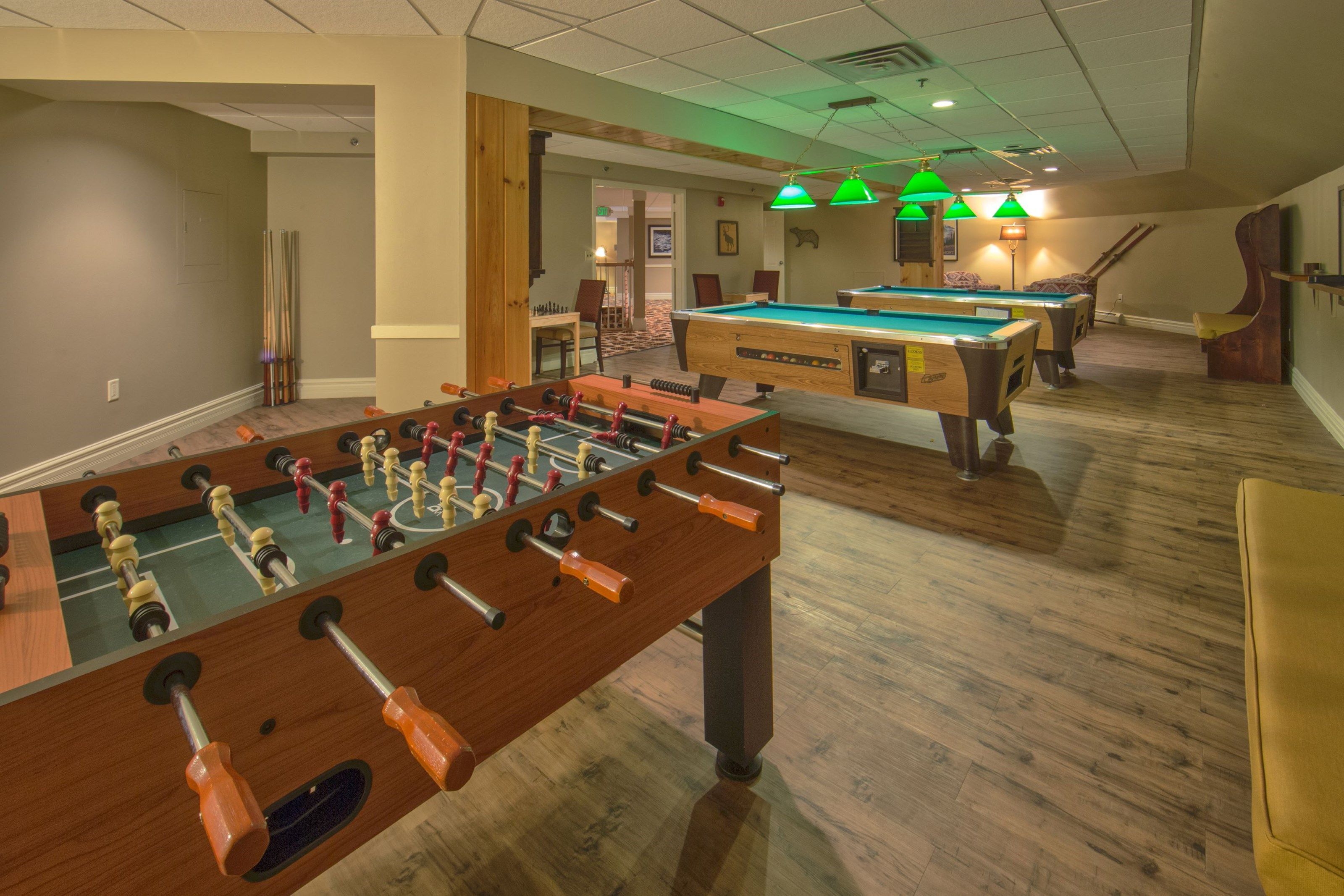 Une pièce avec un baby-foot et une table de billard, un plancher en bois et des suspensions vertes.