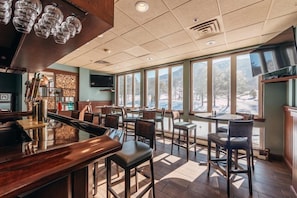 A restaurant with a bar area, high chairs, and a large window offering a view of the outdoors.