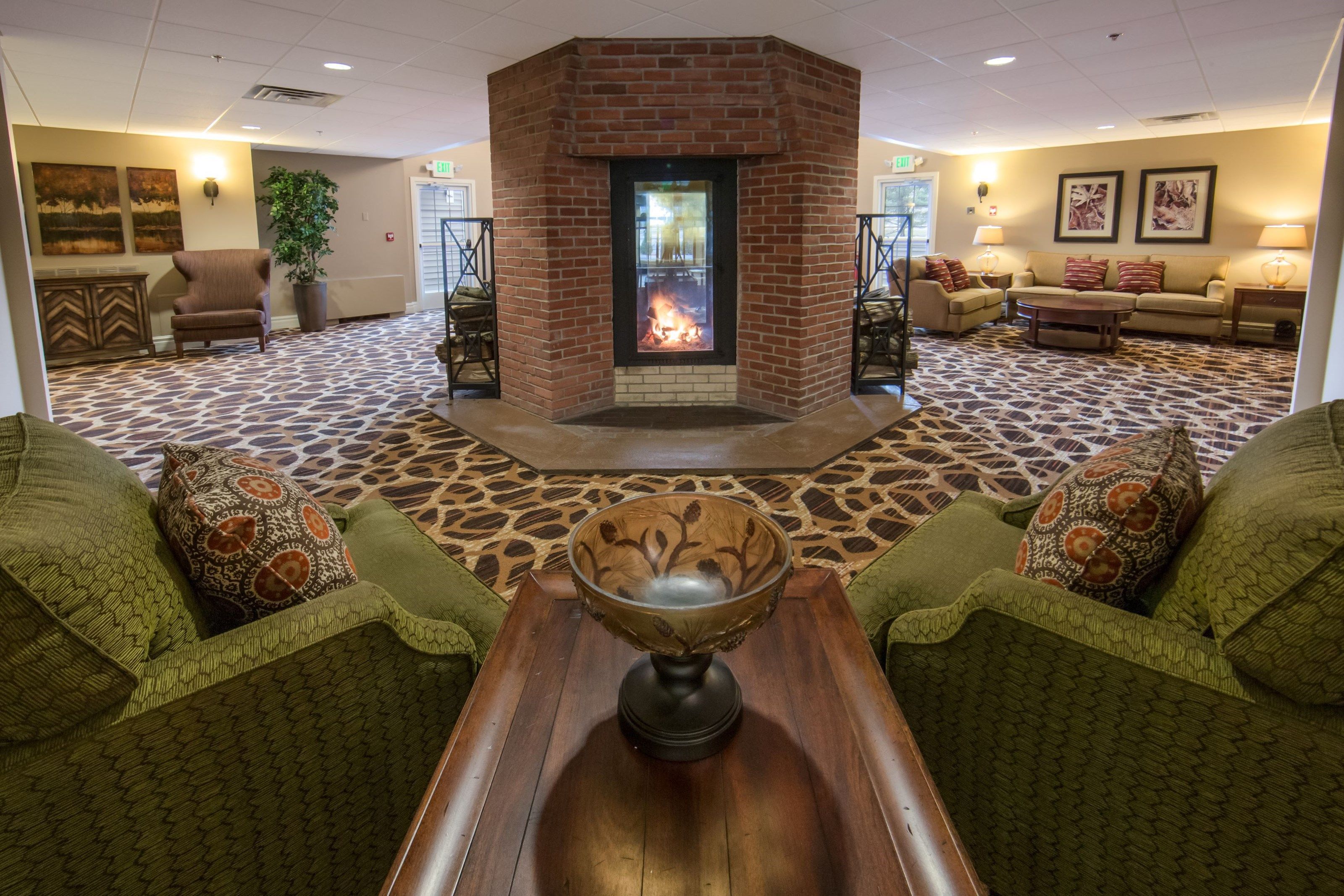 A lobby with a fireplace, green patterned furniture, and a patterned carpet.