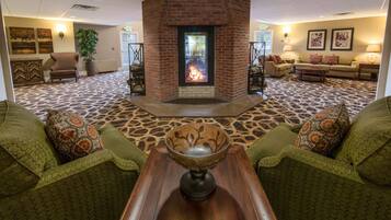 A lobby with a fireplace, green patterned furniture, and a patterned carpet.