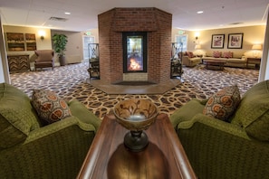 A lobby with a fireplace, green patterned furniture, and a patterned carpet.