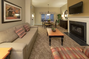 A living room with a sofa, a coffee table, a fireplace, and a television mounted on the wall.